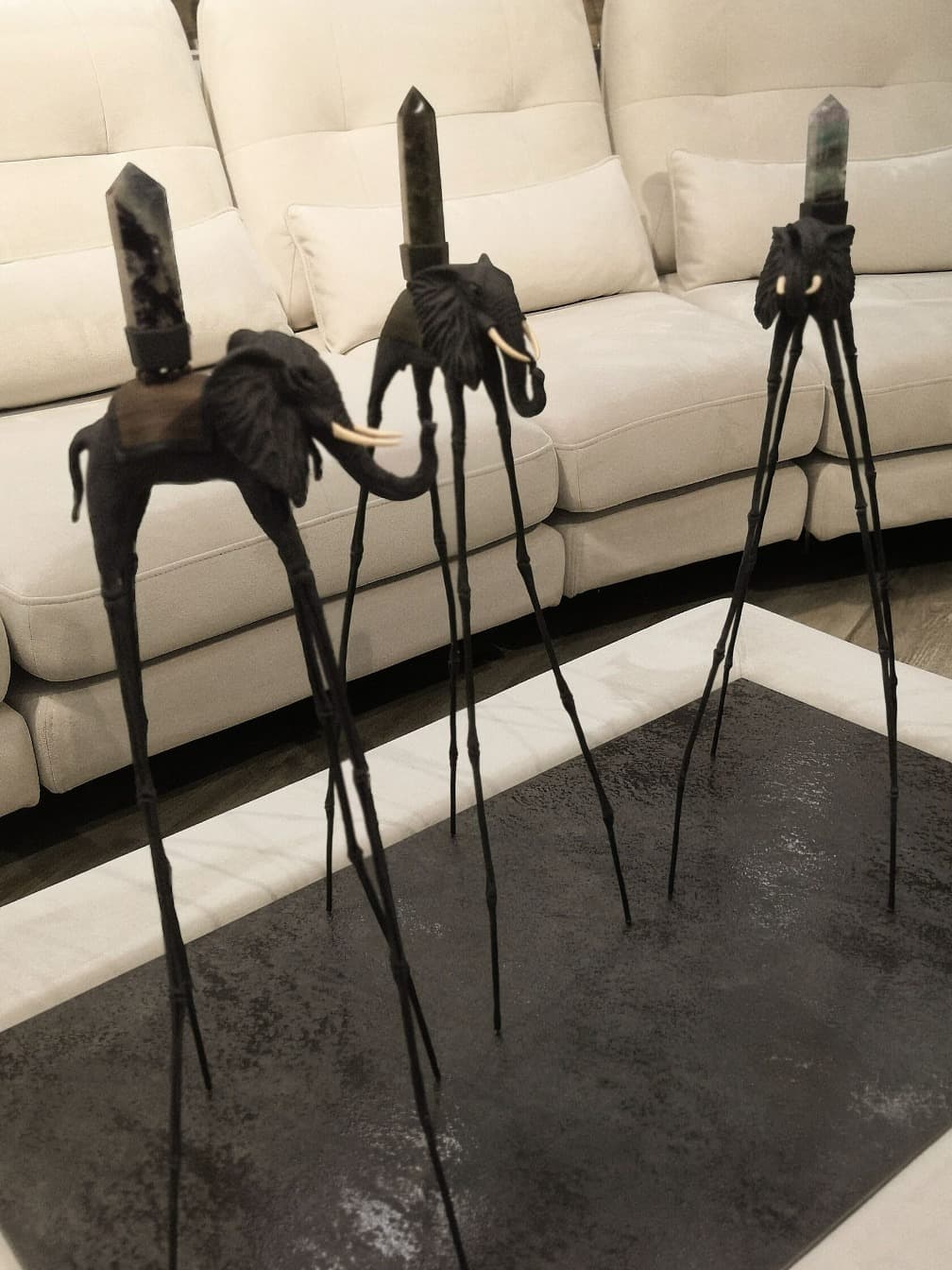 Синие статуэтки слона Дали с натуральными камнями на фоне дивана — декор в стиле Сальвадора Дали